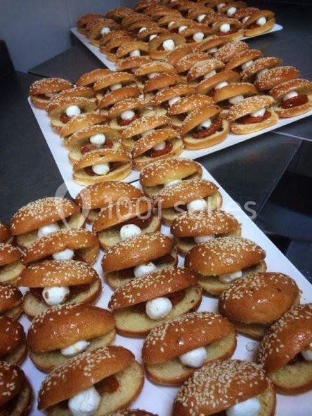 Plateaux de mini-burgers garnis de fromage et de sauce, disposés en rangées sur une surface de préparation.