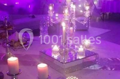 Salle de réception décorée avec des lumières violettes, une arche florale et des chaises transparentes disposées autour de…