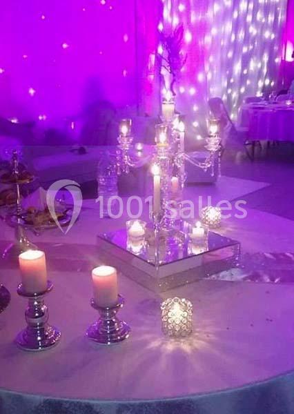 Centre de table avec chandeliers et bougies allumées, entouré de décorations lumineuses dans une ambiance violette.
