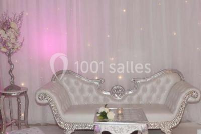 Salle de réception décorée avec des lumières violettes, une arche florale et des chaises transparentes disposées autour de…