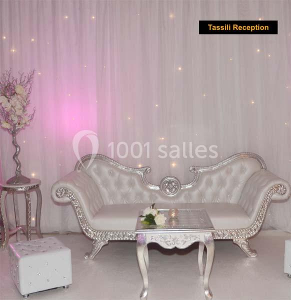 Canapé blanc et argenté avec table assortie, décoré de fleurs et éclairé par des lumières tamisées sur un fond drapé.