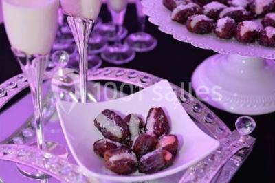 Salle de réception décorée avec des lumières violettes, une arche florale et des chaises transparentes disposées autour de…
