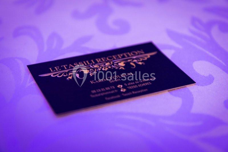 Carte de visite noire avec texte doré posée sur une nappe violette à motifs.