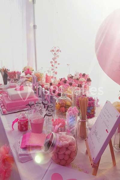 Table décorée avec des desserts, bonbons et macarons roses, accompagnée de ballons et d'une pancarte écrite à la main.