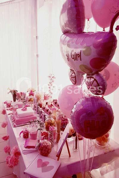 Décoration de fête avec ballons roses, table garnie de douceurs, gâteaux et accessoires pour une célébration.
