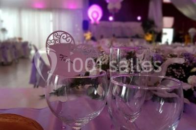 Salle de réception décorée avec des lumières violettes, une arche florale et des chaises transparentes disposées autour de…