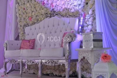 Salle de réception décorée avec des lumières violettes, une arche florale et des chaises transparentes disposées autour de…