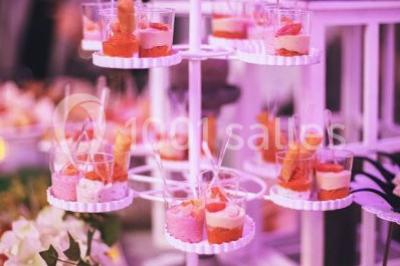 Salle de réception décorée avec des lumières violettes, une arche florale et des chaises transparentes disposées autour de…
