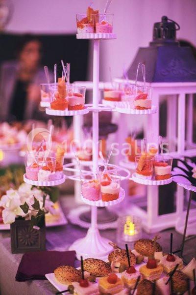 Présentoir à étages avec verrines colorées et table garnie de petits sandwichs, décorée de fleurs et d'une lanterne.