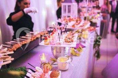 Salle de réception décorée avec des lumières violettes, une arche florale et des chaises transparentes disposées autour de…