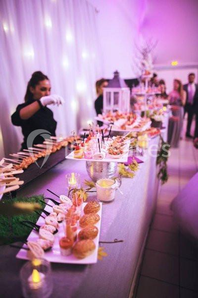 Buffet de réception avec divers amuse-bouches présentés sur une table décorée, éclairage rose en arrière-plan.