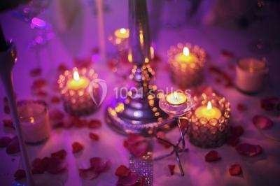 Salle de réception décorée avec des lumières violettes, une arche florale et des chaises transparentes disposées autour de…