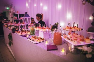 Salle de réception décorée avec des lumières violettes, une arche florale et des chaises transparentes disposées autour de…