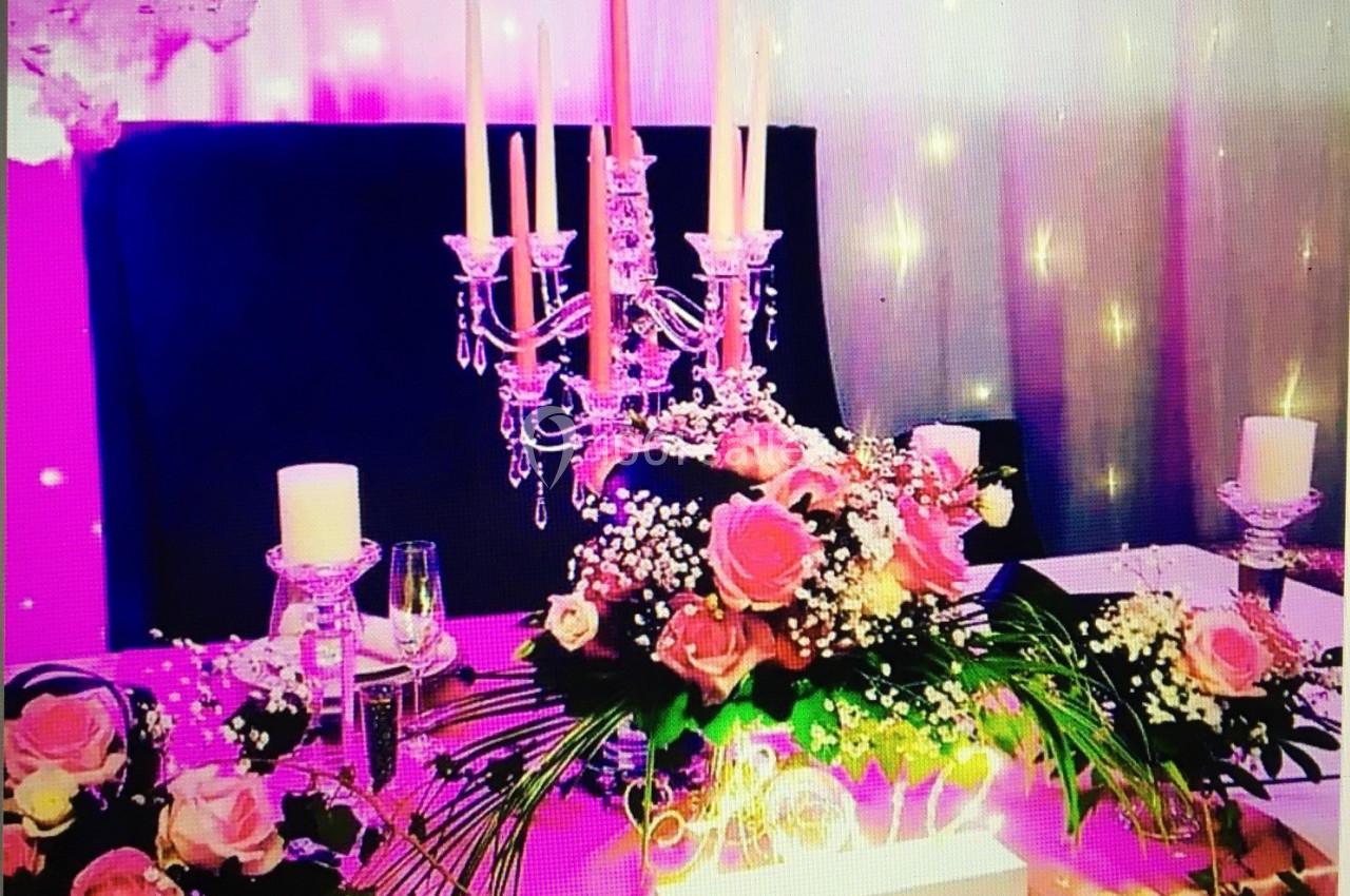 Table décorée avec des roses, un chandelier argenté, des bougies et un éclairage rose en arrière-plan.