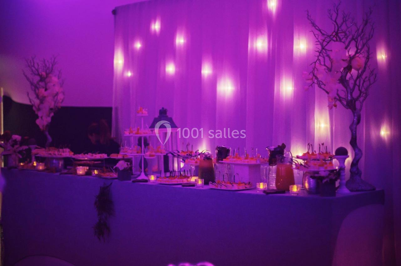 Buffet décoré avec des lumières tamisées violettes, comprenant des boissons et des amuse-bouches sur une table élégante.