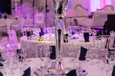 Salle de réception décorée avec des lumières violettes, une arche florale et des chaises transparentes disposées autour de…