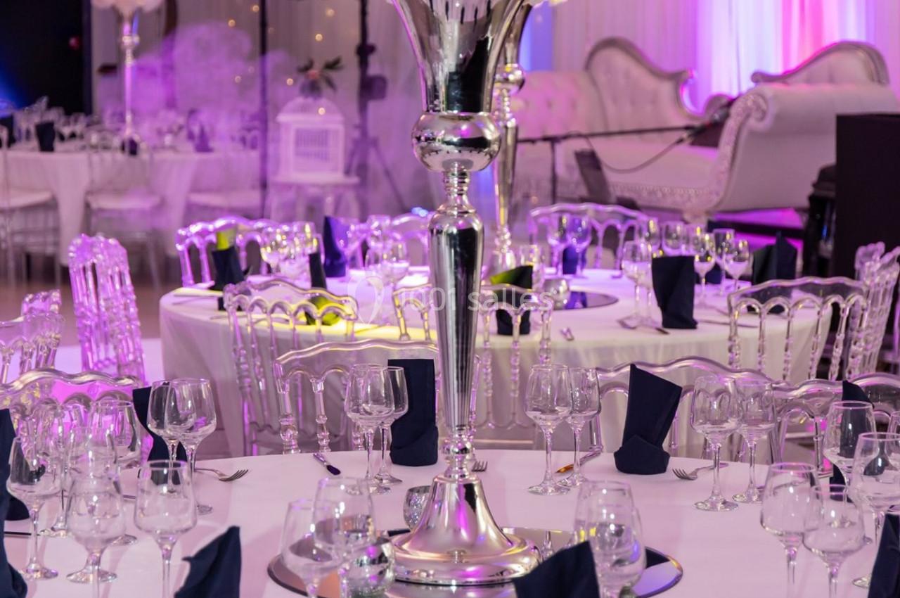 Salle de réception décorée avec des tables élégantes, des chaises transparentes et un centre de table floral sur pied…