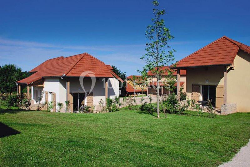 Maisons avec toits en tuiles rouges entourées de pelouses et d'arbres sous un ciel bleu dégagé.