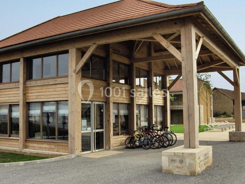 Bâtiment en bois avec toit en tuiles, abritant un espace pour vélos stationnés devant l'entrée vitrée.