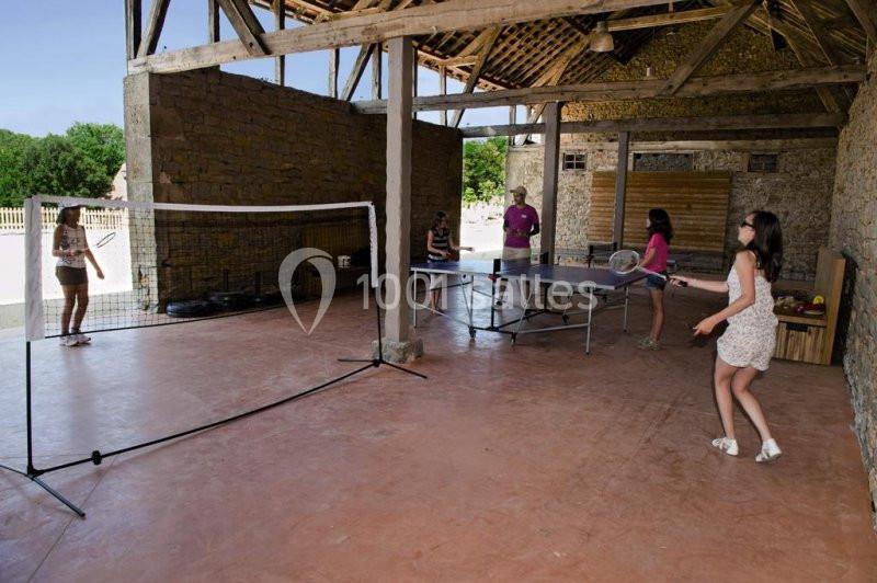 Des personnes jouent au badminton et au tennis de table dans un espace couvert en pierre avec un sol en béton.