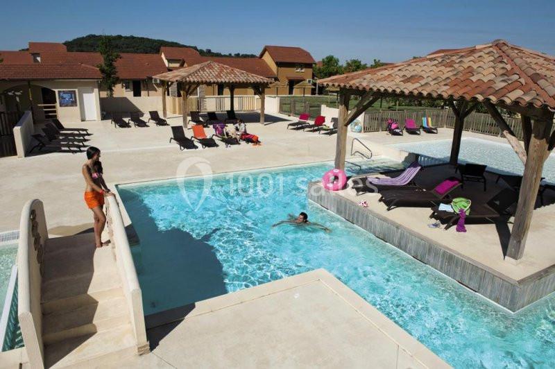 Piscine extérieure avec transats, pergola en bois et baigneurs, entourée de bâtiments aux toits en tuiles.