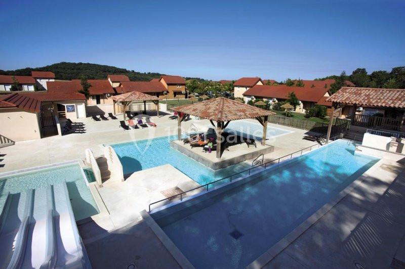 Vue d'un espace aquatique extérieur avec piscines, toboggans et pergolas, entouré de bâtiments aux toits rouges.