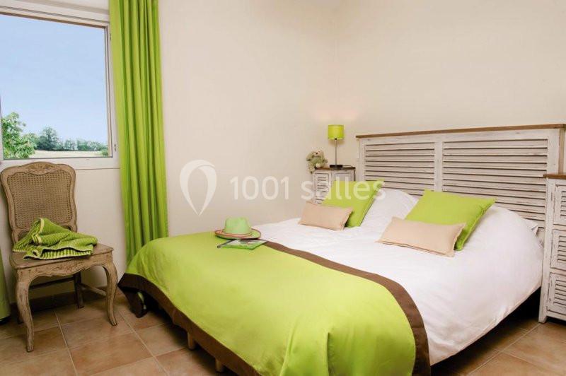 Chambre lumineuse avec lit double, draps verts, mobilier en bois blanc et fenêtre donnant sur un paysage verdoyant.