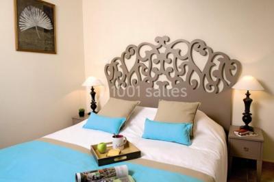 Lit double avec tête de lit décorative, coussins beige et bleu, tables de chevet avec lampes et décoration murale.