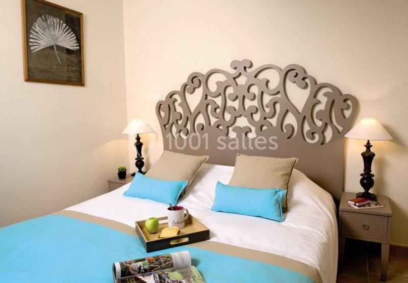 Lit double avec tête de lit décorative, coussins beige et bleu, tables de chevet avec lampes et décoration murale.