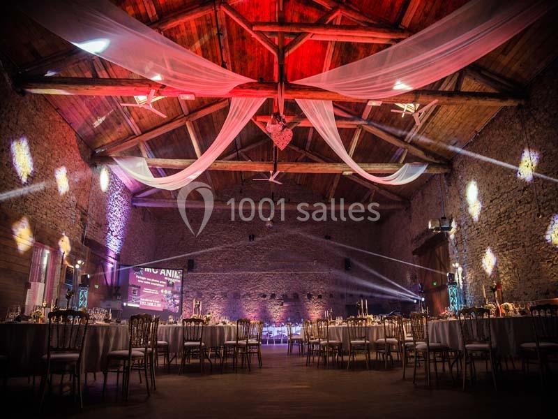 Salle de réception en pierre avec plafond en bois, drapés suspendus et tables décorées pour un événement.