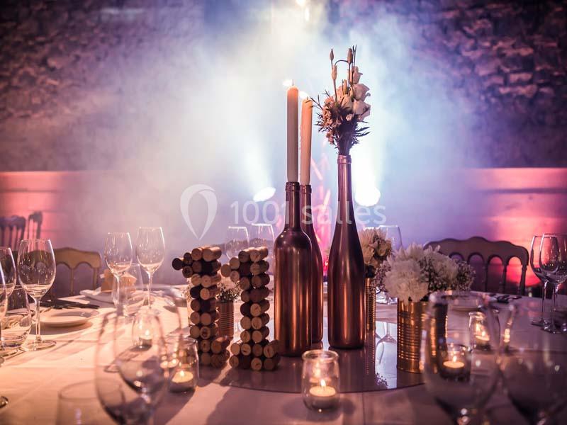 Centre de table avec bougies, fleurs et bouteilles décoratives, entouré de verres et d'assiettes dans une ambiance tamisée.