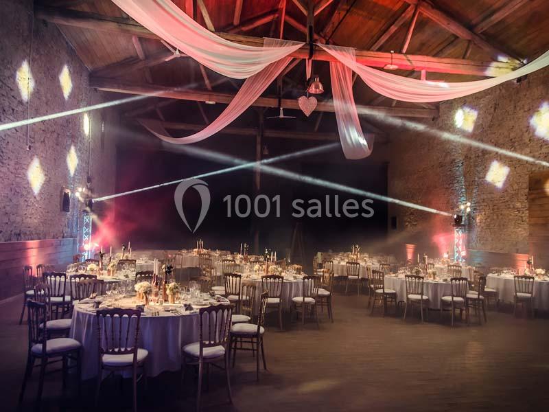 Salle de réception décorée avec des tables rondes dressées, éclairages colorés et voilages suspendus au plafond.