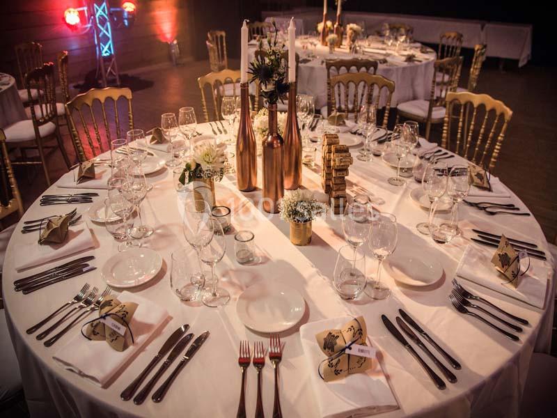 Table ronde élégamment dressée avec nappes blanches, couverts, verres, bougies et décorations florales.