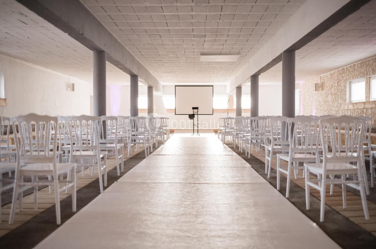 Salle lumineuse avec rangées de chaises blanches alignées face à un écran de projection.