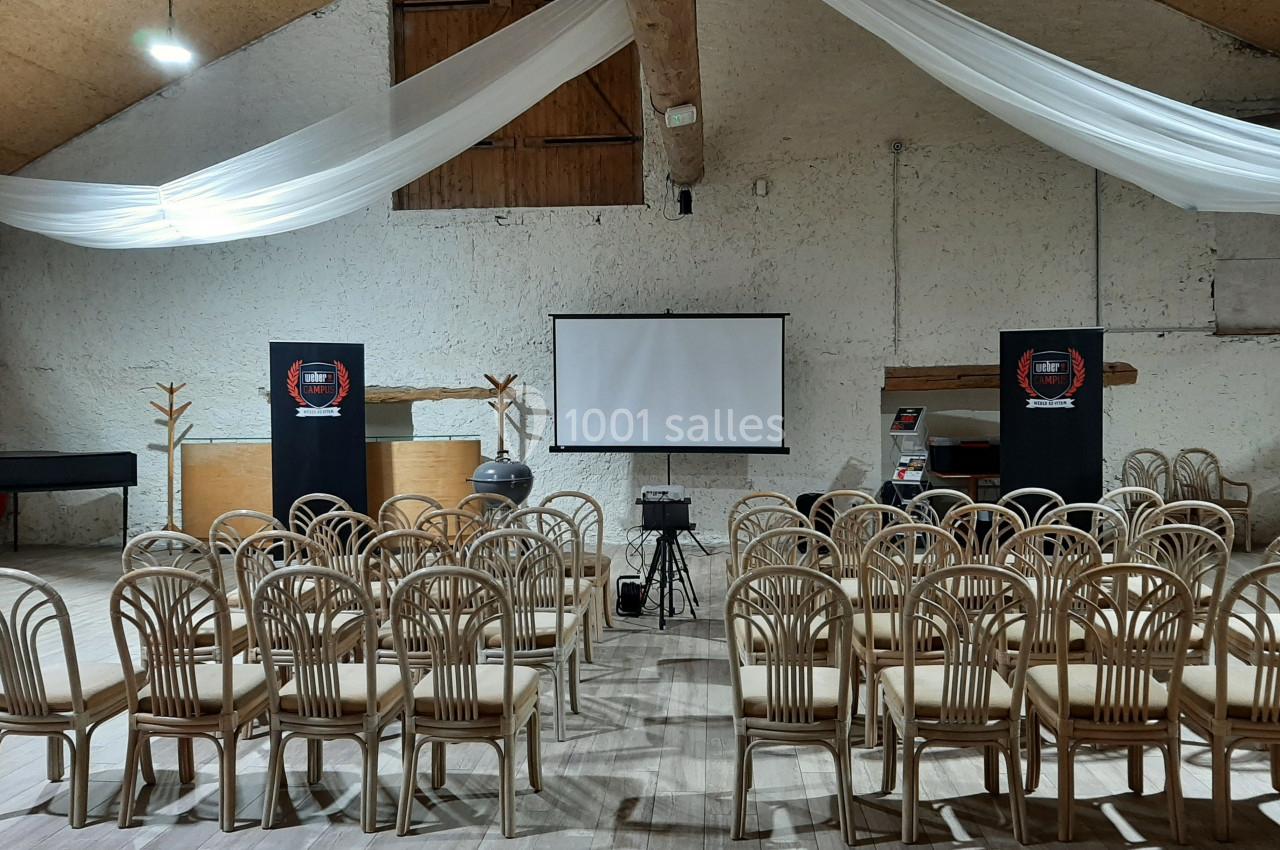 Salle de conférence avec chaises alignées, écran de projection, projecteur et décoration sobre sous un plafond en bois.
