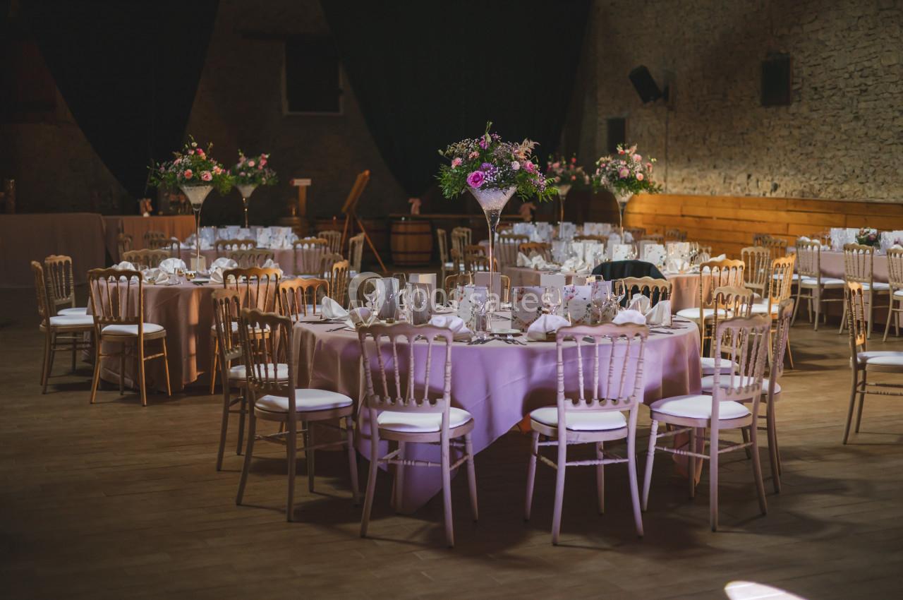 Salle de réception décorée avec des tables rondes nappées de rose, chaises en bois clair et arrangements floraux.