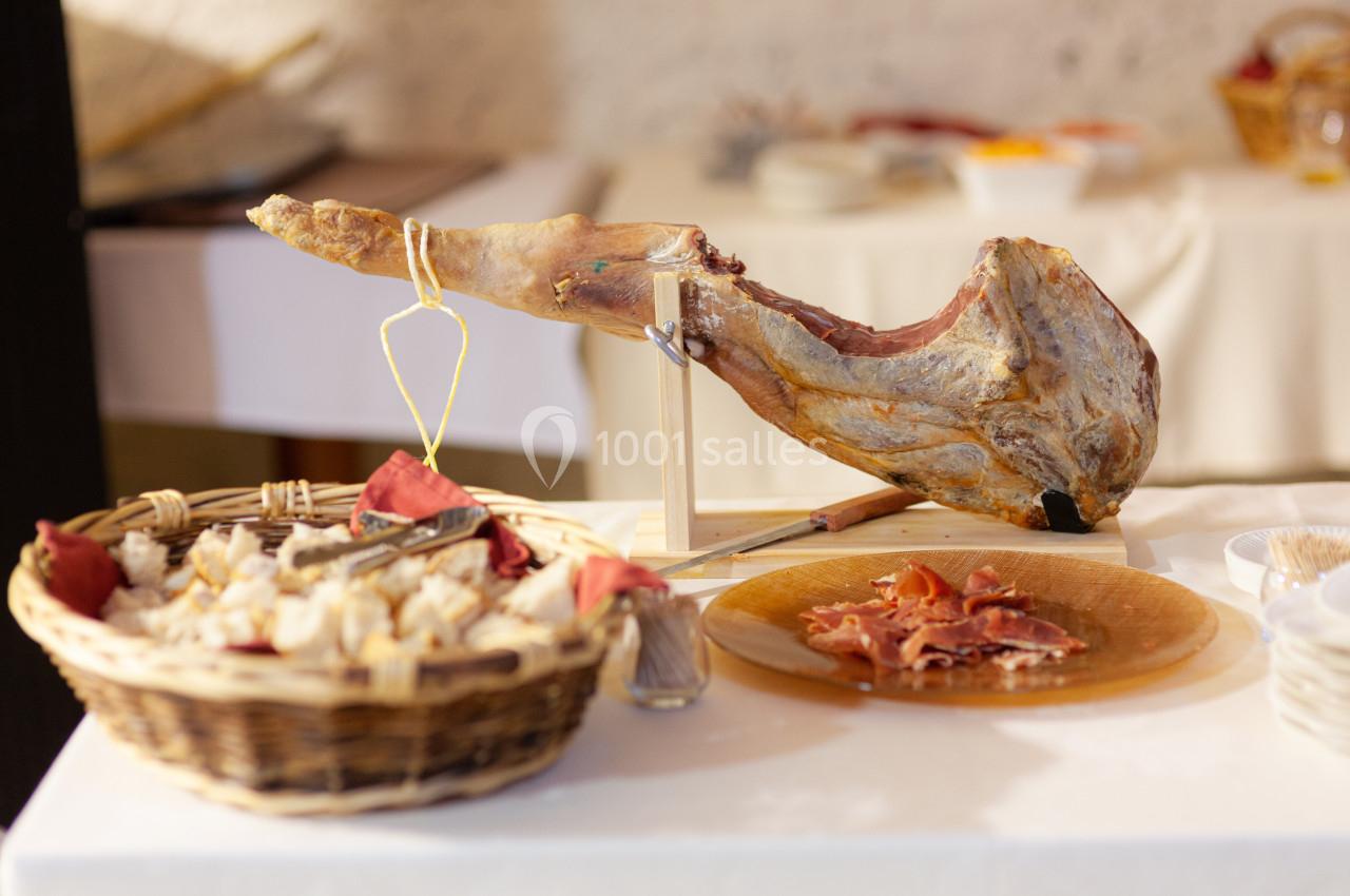 Jambon entier sur support avec tranches coupées, accompagné d'un panier de pain sur une table blanche.