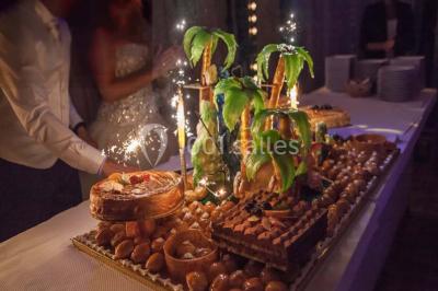 Allée avec tapis rouge menant à une arche décorée de fleurs, dans un espace extérieur ensoleillé.