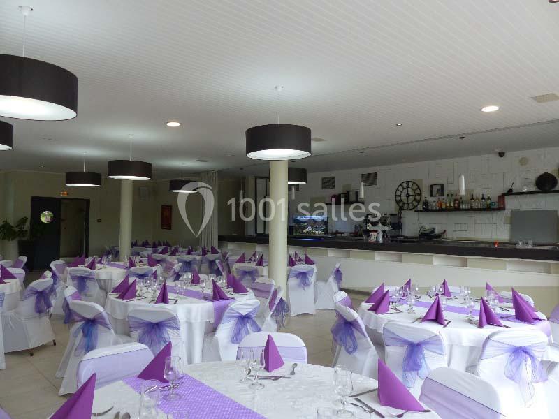 Salle de réception décorée avec des nappes blanches, des serviettes violettes et des chaises ornées de nœuds assortis.