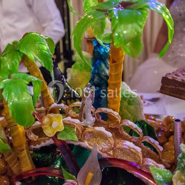 Pièce montée décorative avec des palmiers en sucre coloré, une cascade et des détails comestibles élaborés.