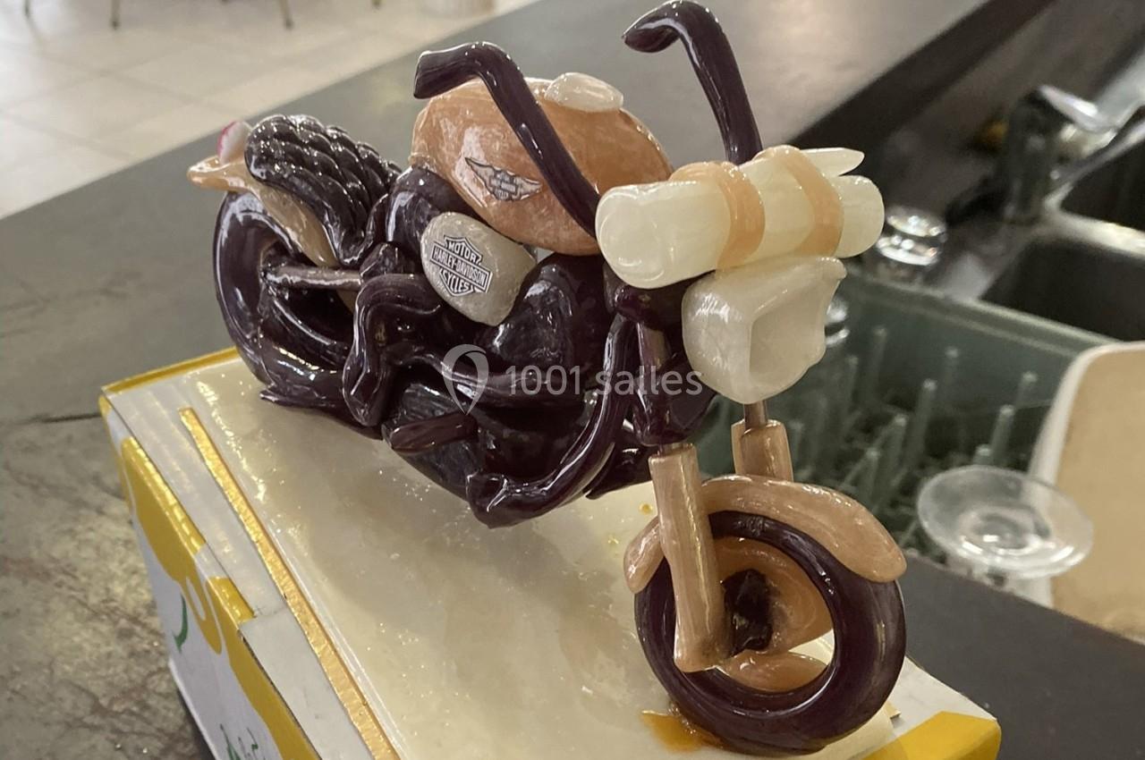 Sculpture miniature d'une moto réalisée en sucre coloré, exposée sur un socle dans un environnement intérieur.