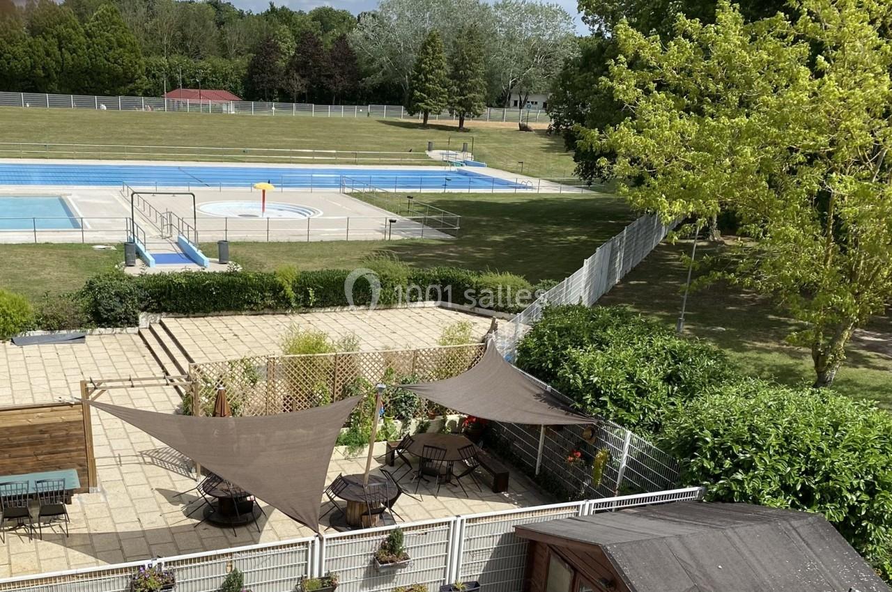 Vue d'une terrasse ombragée avec des voiles, donnant sur une piscine extérieure et un espace vert arboré.