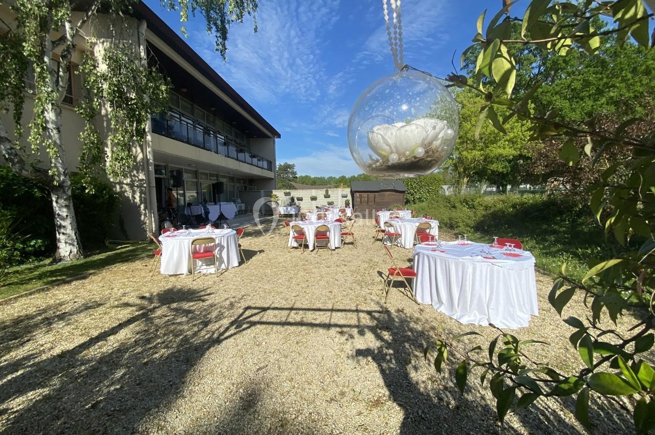 Tables dressées en extérieur avec nappes blanches et chaises rouges, devant un bâtiment moderne sous un ciel dégagé.