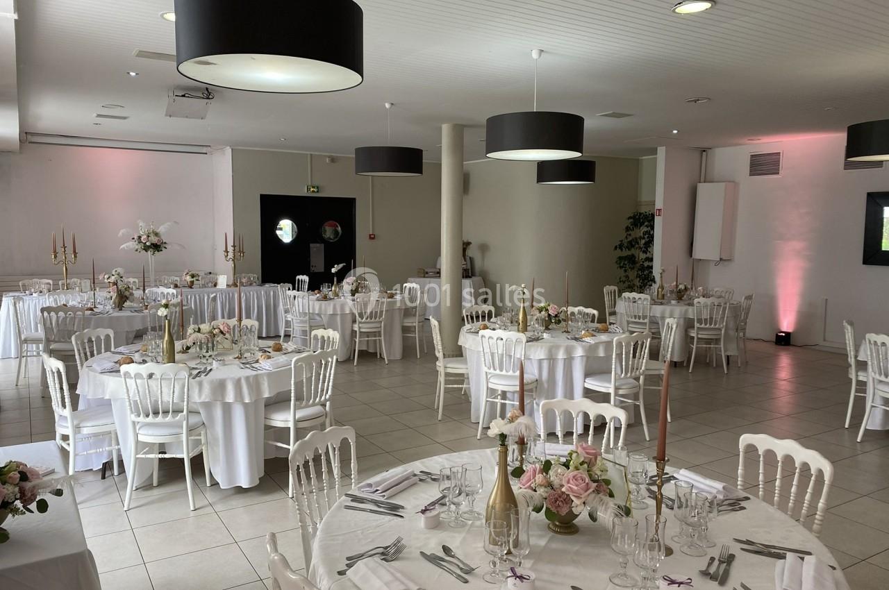 Salle de réception décorée avec des tables rondes, nappes blanches, chaises élégantes et arrangements floraux.