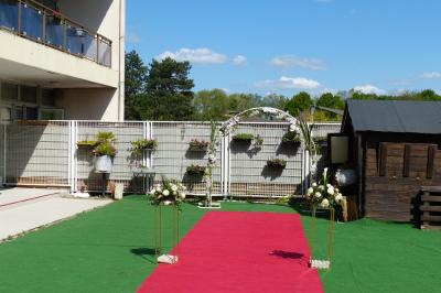 Allée avec tapis rouge menant à une arche décorée de fleurs, dans un espace extérieur ensoleillé.