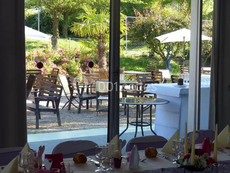 Salle de réception avec vue sur une terrasse aménagée, entourée de verdure et de mobilier de jardin en bois.