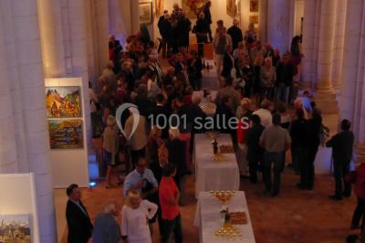 Salle avec des chaises rouges alignées, une table avec des micros, un écran de projection et des bannières promotionnelles.