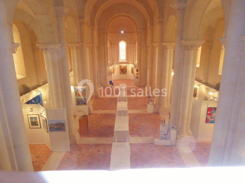 Vue intérieure d'une église transformée en espace d'exposition, avec des œuvres d'art accrochées le long des murs.