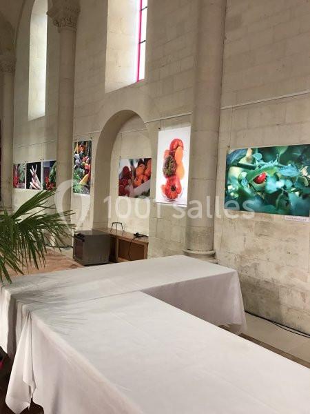 Exposition de photographies de fruits et légumes accrochées sur un mur en pierre dans une salle lumineuse.