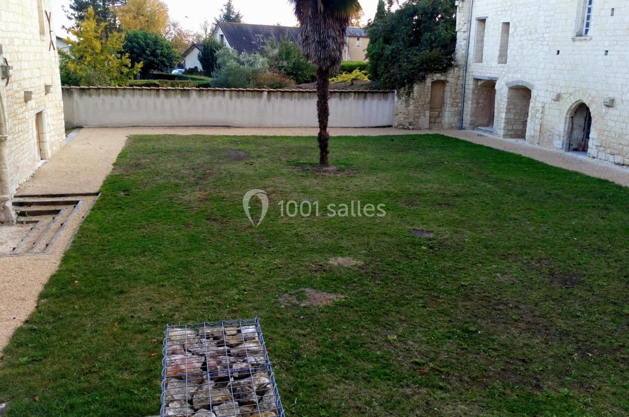 Cour intérieure avec pelouse, palmier central, murs en pierre blanche et bâtiments anciens en arrière-plan.